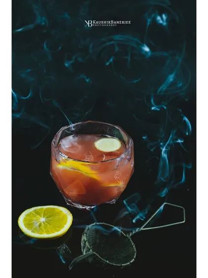 A smoky citrus cocktail against a dark, moody background. I use techniques like smoke to add drama and atmosphere, creating an alluring image for a bar's specialty drink menu.