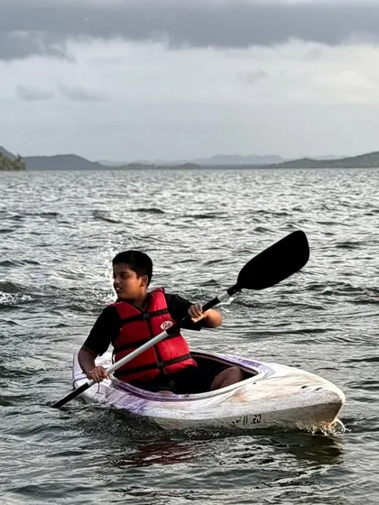 A young participant confidently paddles his kayak, while others swim nearby. Our camps are designed to build water confidence in a fun and supervised environment.