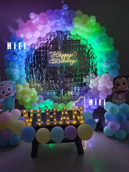 A Cocomelon themed first birthday with a rainbow balloon arch and a shimmering backdrop.