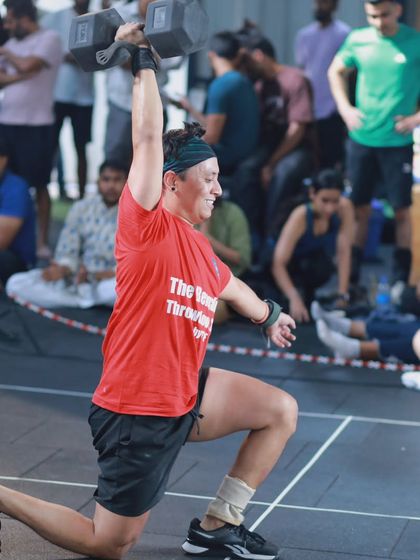 A competitor performs a dumbbell overhead lunge, a movement that challenges stability, strength, and coordination all at once.