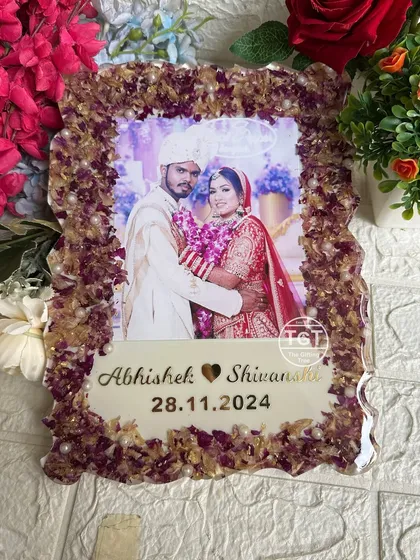 A 9x12 inch resin photo frame with a border made from preserved varmala flowers and gold flakes. The couple's photo is centered above their names and wedding date.