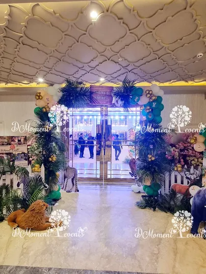 The entrance to Yunay's safari party, featuring a variety of 3D animal props like a zebra, lion, and elephant, set among lush greenery.