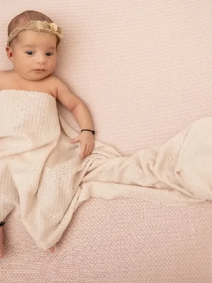 Elegantly draped in a cream-colored wrap against a soft pink background. This portrait highlights the baby's delicate features and serene expression in a minimalist setting.