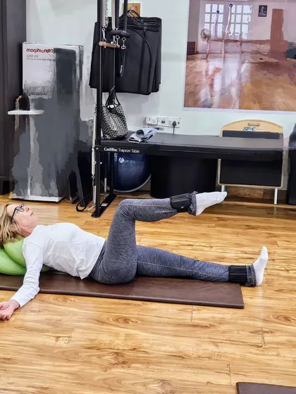 A client performing a mat exercise with ankle weights and a stability cushion for head support. Small props can make a big difference.