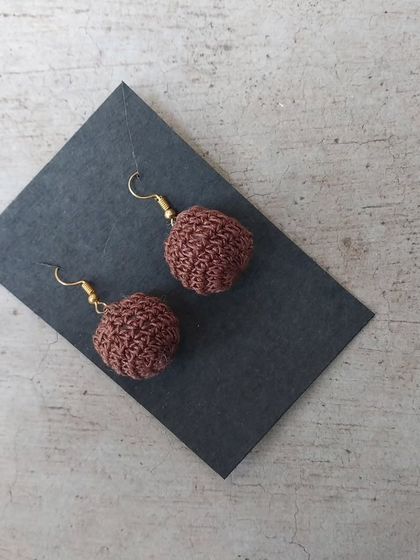 A close-up shot of the brown crochet ball earrings, showing the texture of the stitch.