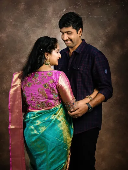 A classic maternity portrait of a couple in traditional Indian attire. The mom-to-be wears a vibrant turquoise and pink silk saree, showcasing the elegance of a traditional pregnancy photoshoot.