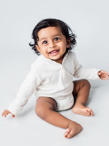 A happy baby boy sitting up in the studio, captured against a simple grey background.