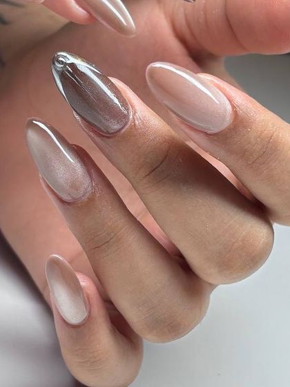 A modern and chic manicure featuring a nude cat-eye base with a single, sculpted silver chrome accent. The mix of textures is subtle yet striking.