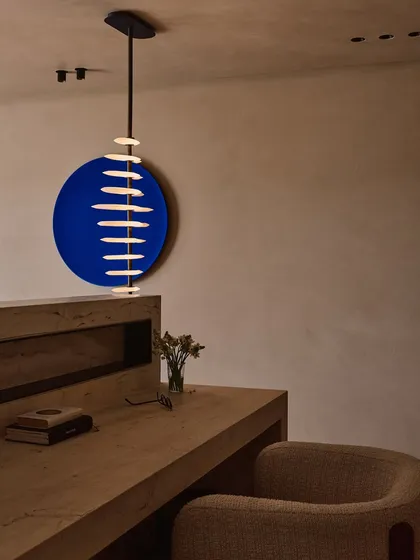 This study area features a bold blue circular art piece that contrasts beautifully with the minimalist wooden desk. The suspended pendant light adds another layer of sculptural interest, turning a simple corner into a design statement.