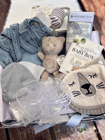This hamper is all about cozy textures and gentle friends, featuring a denim romper, a plush teddy bear, and an adorable lion-faced bib for a baby boy.