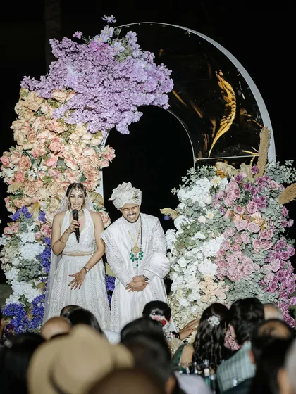 The bride and groom addressing their guests during the reception. This photo captures a moment of gratitude and shared happiness in front of a beautiful floral backdrop.