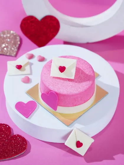 A lovely pink Valentine's Day cake decorated with edible love letters and hearts. The monochromatic pink and white styling creates a sweet and romantic mood.
