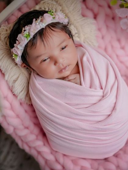 A little blossom. This baby, swaddled in pink, is resting on a miniature bed surrounded by delicate pink flowers.