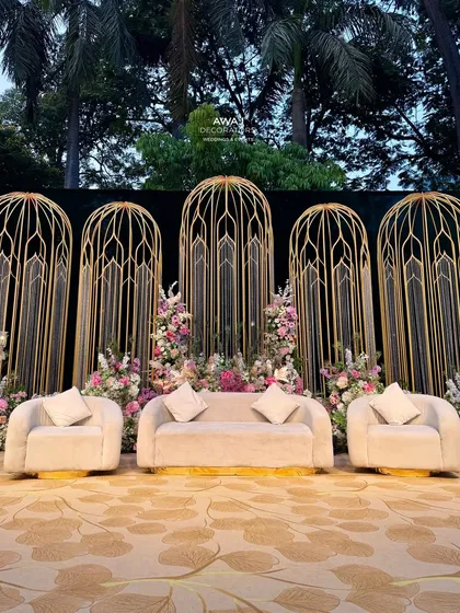 A direct view of the stage, highlighting the plush cream-colored sofas set against the intricate gold backdrop and surrounded by a garden of pastel flowers.