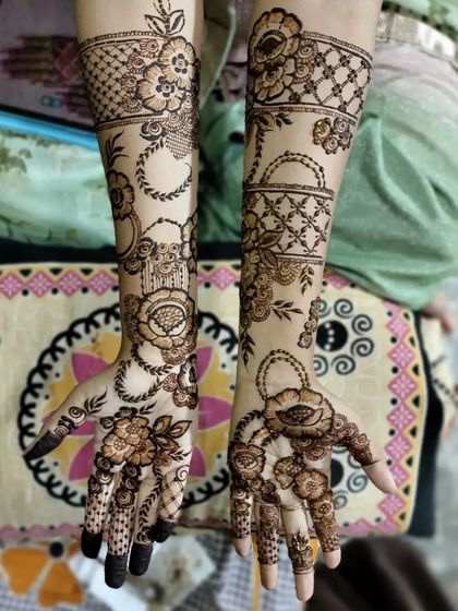 This design features unique hanging basket motifs on the wrists, filled with flowers. The rest of the hands are covered in a mix of vines and traditional patterns.