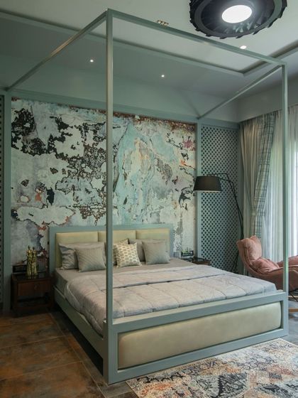 An artistic bedroom featuring a four-poster bed and a dramatic, textured accent wall that resembles aged plaster. The soft color palette of sage green and dusty rose creates a space that is both eclectic and calming.
