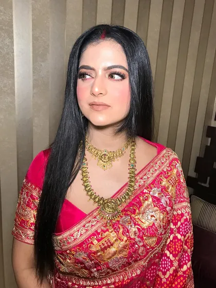 A close-up of the client in the red saree, her layered gold temple necklace the perfect accessory.