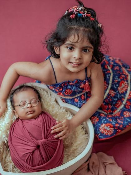 Two siblings, one heart. I love the sweet curiosity and gentle care as this big sister looks after her new baby brother, nestled in a heart-shaped basket.