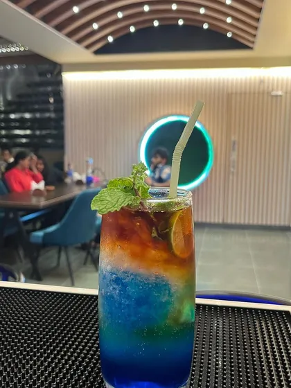 The Blue Moon mocktail is a visual treat. This vibrant, multi-layered citrus drink is served over ice with a mint garnish, offering a crisp and refreshing taste that pairs well with any dish.
