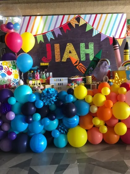 A vibrant and creative art-themed party for Jiah. This colorful setup features a rainbow balloon garland, a chalkboard-style backdrop, and giant crayon props for a fun and inspiring celebration.