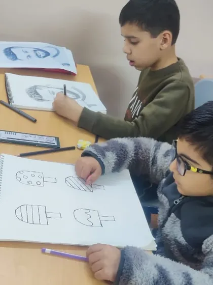 Two boys working side-by-side on their art projects. One is practicing sketching, while the other is drawing different types of ice cream.