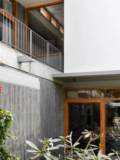 The meeting of materials: raw board-formed concrete, smooth white plaster, and warm teak wood window frames.
