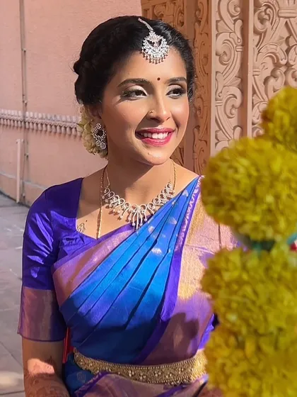 A stunning Veradam look for a Tamil bride. The makeup is understated and unblemished, with a bright lip that complements her vibrant blue and purple saree.