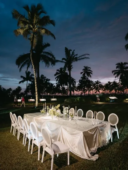 An intimate dinner setting under the dusky Goan sky. The combination of elegant white tablescapes, soft candlelight, and the silhouette of palm trees creates a romantic and timeless atmosphere for a close-knit celebration.