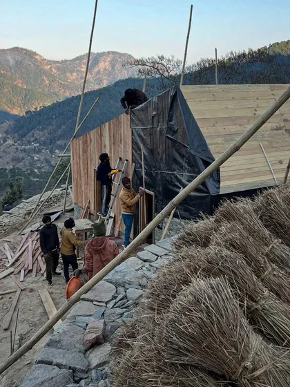 Workers apply wooden cladding and waterproofing to a guesthouse in the Himalayas. This phase of construction is critical for ensuring the building can withstand the region's heavy snow and monsoon seasons.