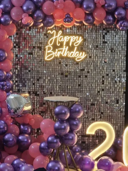A vibrant 26th birthday decoration with a silver sequin wall framed by a pink and purple balloon arch and matching light-up numbers.