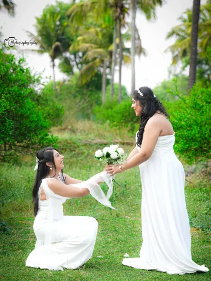 A playful moment between friends, with one kneeling to present a bouquet of flowers to the mother-to-be.