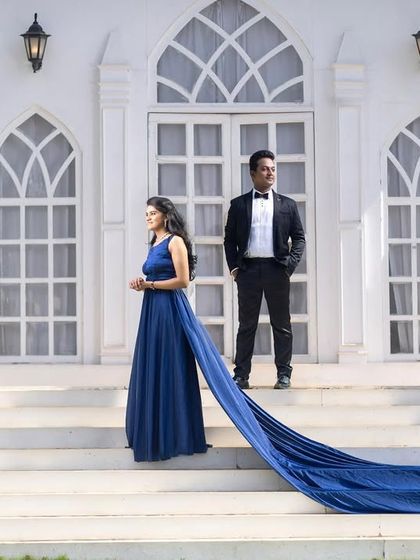 An elegant, formal portrait on the steps of a white chapel set. The long train of the blue dress adds a touch of classic glamour.