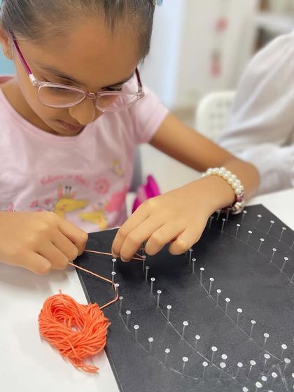 A young girl concentrates as she weaves orange string to create her pumpkin design.