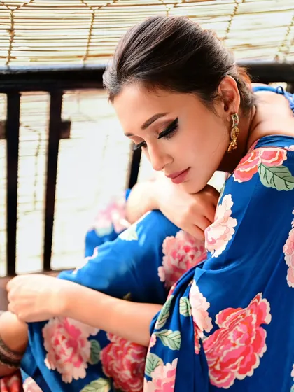 A contemplative portrait of Mimi Chakraborty in a blue floral saree. Her downward glance and the soft, natural light from the window create a quiet and thoughtful mood.