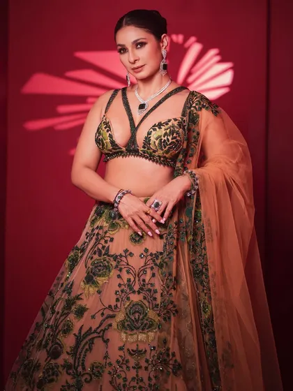 A confident front-facing portrait in a modern, strappy-blouse lehenga. The look is accessorized with a diamond and emerald necklace, showcasing a fusion of traditional and contemporary styles.