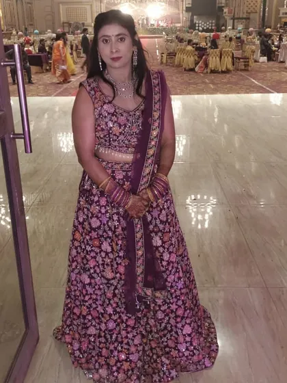 Our happy client posing in a deep purple lehenga with multi-color floral embroidery, a perfect outfit for a wedding guest.