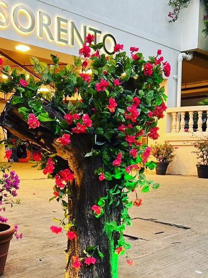 An artificial flowering tree installed outside a hotel entrance. The bright red flowers are wrapped around a real tree trunk for a realistic and eye-catching display.
