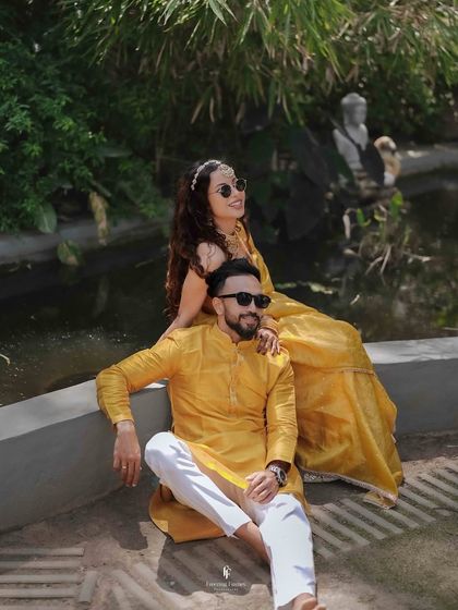 A stylish portrait of the couple posing by a small pond during their Haldi event, both dressed in coordinated yellow outfits.