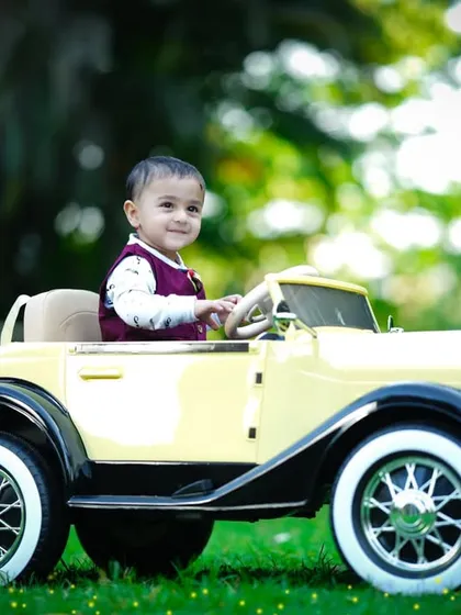 This little boy looks so proud driving his classic car through the grassy field.