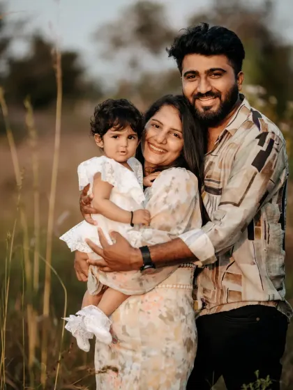 A beautiful family portrait captured outdoors in a natural setting. The genuine smiles and easy embrace showcase the love and connection between the parents and their young daughter, a perfect memory of this chapter in their lives.