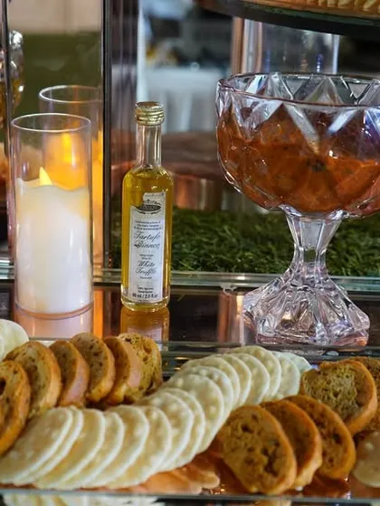 Part of a beautiful grazing table spread, this arrangement includes a variety of crackers and artisanal dips like pesto and sun-dried tomato, presented in elegant crystal bowls.