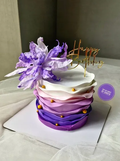 This cake showcases a beautiful purple ombre wave effect in buttercream. Topped with a delicate, handcrafted wafer paper flower, it's a unique and artistic design for any occasion.