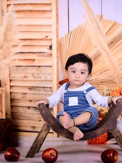 A baby boy sitting in a rustic setup with pampas grass and apples, showcasing a simple yet elegant theme.