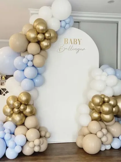 A sophisticated baby shower setup in a neutral palette. The white arched backdrop is framed by balloons in beige, light blue, and gold, offering a calm and elegant aesthetic.