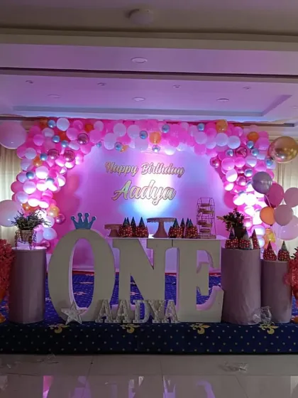 A classic and grand first birthday celebration in pink. This stage decoration features a large balloon arch, a "Happy Birthday" backdrop, and oversized "ONE" letters, creating a perfect setting for cake cutting and photos.