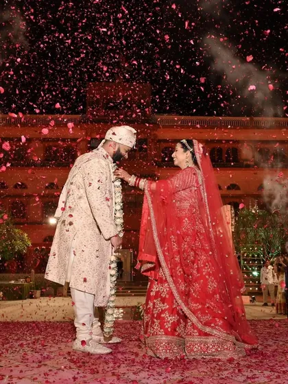 A royal varmala ceremony set against the stunning architecture of a palace in Jaipur. The air filled with rose petals creates a timeless and romantic moment for the couple.