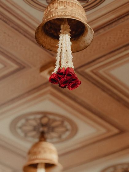 A delicate detail of a brass temple bell with a garland of jasmine and red roses hanging from the mandap ceiling. This small touch adds to the authentic, sacred feel of the ceremony space.