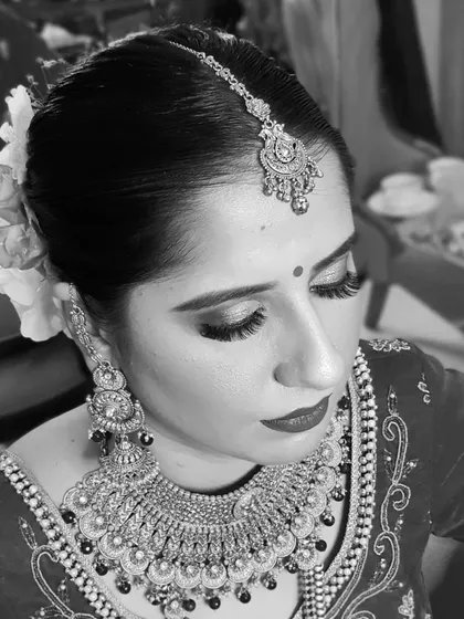 A side-profile portrait in black and white. This angle beautifully showcases the long lashes, the contour of her cheekbones, and the elegant floral hair bun.
