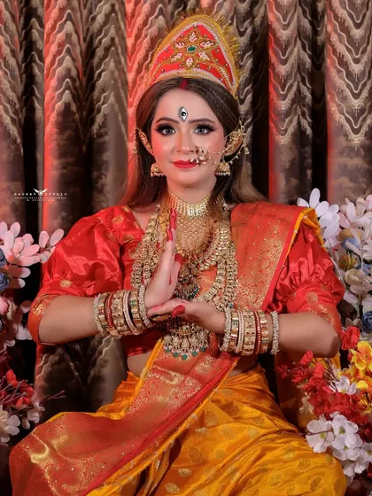 The model poses with hands in a namaste gesture, surrounded by flowers, completing the divine look.