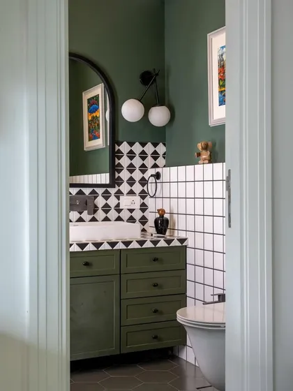 A peek into a bathroom from the 'Inde Blue' project reveals a space rich in color and pattern. The olive green vanity, geometric tiles, and modern globe lighting create a look that is bold, graphic, and full of personality.